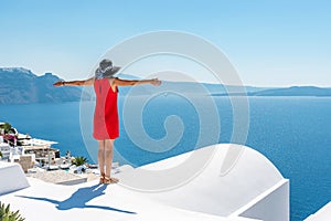 Woman in red dress on the roof enjoying view of Santorini island and Caldera in Aegean sea.