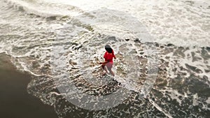 Woman in red dress running in water by sand beach on the seaside on sunset, inspirational freedom happy holidays concept