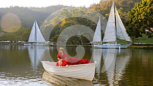 Woman in red dress sailing on wooden boat against sunset at mountain top. Romantic scene of perfect date