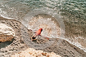 Woman red dress sea. Female dancer in a long red dress posing on a beach with rocks on sunny day