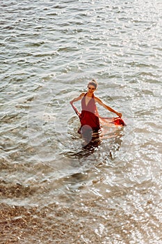 Woman red dress sea. Female dancer in a long red dress posing on a beach with rocks on sunny day