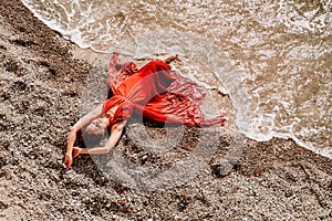 Woman red dress sea. Female dancer in a long red dress posing on a beach with rocks on sunny day