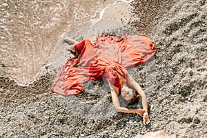 Woman red dress sea. Female dancer in a long red dress posing on a beach with rocks on sunny day