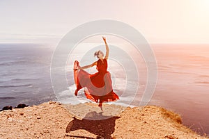 Woman red dress sea. Female dancer in a long red dress posing on a beach with rocks on sunny day. Girl on the nature on