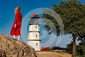 A woman in a red dress is standing on the beach near the lighthouse at sunrise