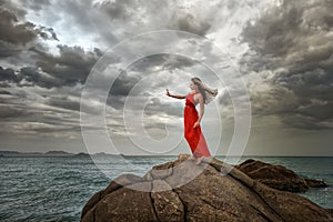 Woman in red dress stands on a cliff with a beautiful sea view a