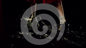 Woman in red dress and summer shoes walking on puddled floor of a dark stage. Stock footage. Dramatic theatre scene with