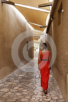 A woman in a red dress walking on a narrow street in Bastakia area of old town Dubai