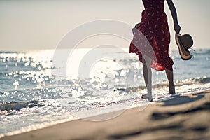 Woman in red dress walking on the beach at sunset