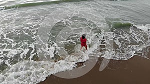 Woman in red dress walking into the water by sand beach on the seaside on sunset, inspirational freedom happy holidays