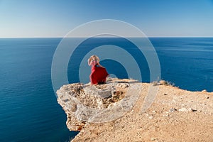 A woman in a red flying dress fluttering in the wind, against the backdrop of the sea.