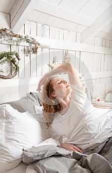 Woman with red hair in bed in a bright room with a Christmas interior, wakes up, morning