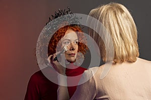 Woman with red hair doing makeup Beautician, applying powder to her face with a large brush, powdering the skin, selective focus.