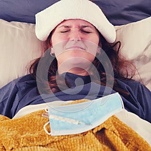 Woman with red hair lies in bed sick with coronavirus with a cold compress on her head