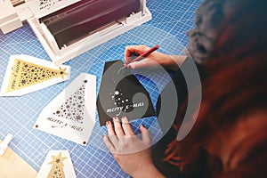 woman with red hair and painted nails works on christmas graphic cut from black vinyl foil