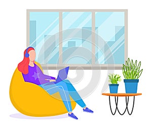 Woman red hair sitting yellow beanbag using laptop, indoor large window, modern workspace