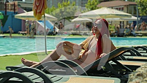 A woman with red hair sunbathes on a sun lounger by the pool