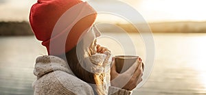 Woman in a red hat is drinking coffee on the lake at sunset. Autumn outdoor recreation. Concept of freedom of travel