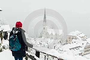 Woman in red hat enjoying the view over Hallstatt old town during snow storm, Austria