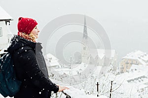 Woman in red hat enjoying the view over Hallstatt old town during snow storm, Austria