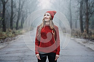 Woman in red hat and sweater walking on foggy mystical morning forest.