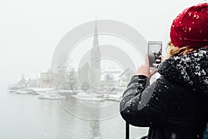 Woman in red hat taking picture of Hallstatt old town during snow storm, Austria