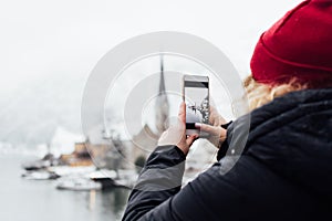 Woman in red hat taking picture of Hallstatt old town during snow storm, Austria