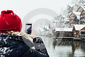 Woman in red hat taking picture of Hallstatt old town during snow storm, Austria