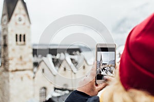 Woman in red hat taking picture of Hallstatt old town during snow storm, Austria