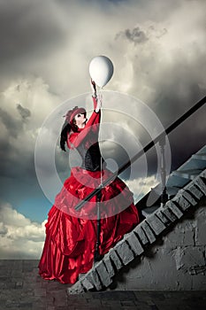 Woman in a red historical dress is catching a white balloon.