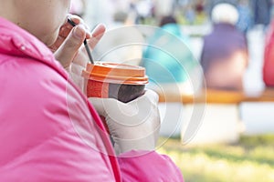 A woman in a red jacket drinking coffee through a tube