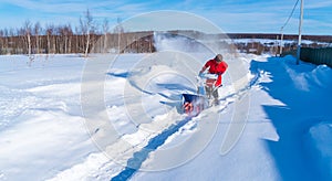 A woman in a red jacket removes snow from a rural road with a snowblower in winter after a snowfall