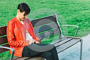 Woman with red jacket sitting on a bench with smartphone