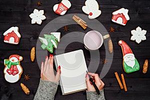 Woman with red manicure writing New year resolutions in blank notebook, copy space. Christmas background with gingerbread cookies.