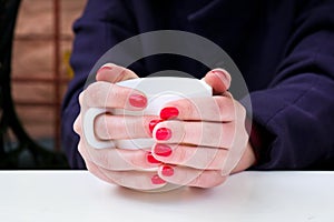 Woman with red nail polish holding white cup in a cafee photo