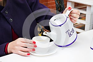 Woman with red nail polish pouring a tee in a cup in a cafee photo