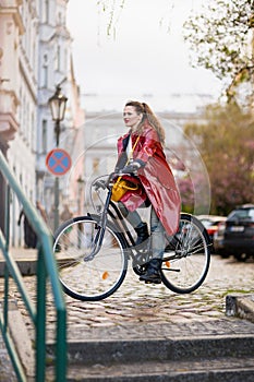 Woman in red rain coat outdoors on city street riding bicycle