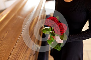 Woman with red roses and coffin at funeral