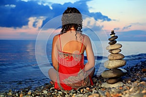 Woman in red sitting near to pyramid from pebble