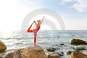 A woman in a red suit practicing yoga on stone at sunrise near the sea