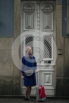 Woman with a red suitcase stands at the front doors, Porto, Portugal.