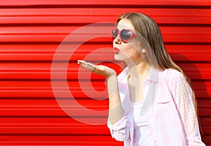 Woman in red sunglasses sends an air kiss over colorful