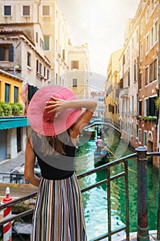 Woman with red sunhat enjoys the view to a canal in Venice, Italy