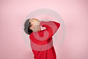 Woman in red sweater covering her face with hands. Concept of fear, shame, domestic violence.