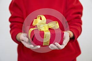 A woman in a red sweater holds a red Christmas present on a white background. Gift concept for Christmas and New Year