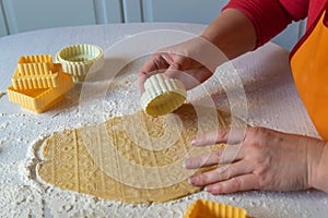 Woman in red sweater and orange apron carves cookies on the dough. Concept of festive Christmas baking