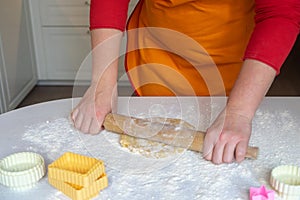 A woman in a red sweater and orange apron rolls out dough on the table. Festive Christmas baking concept