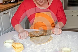 A woman in a red sweater and orange apron rolls out dough on the table. Festive Christmas baking concept