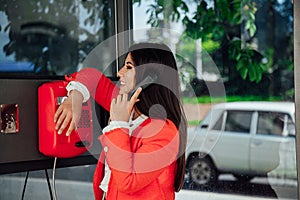 Beautiful woman in red talking on street phone in a phone booth