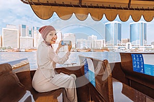 Woman in a red turban takes pictures on her smartphone while cruising on a traditional Abra Dhow boat on Dubai Creek.